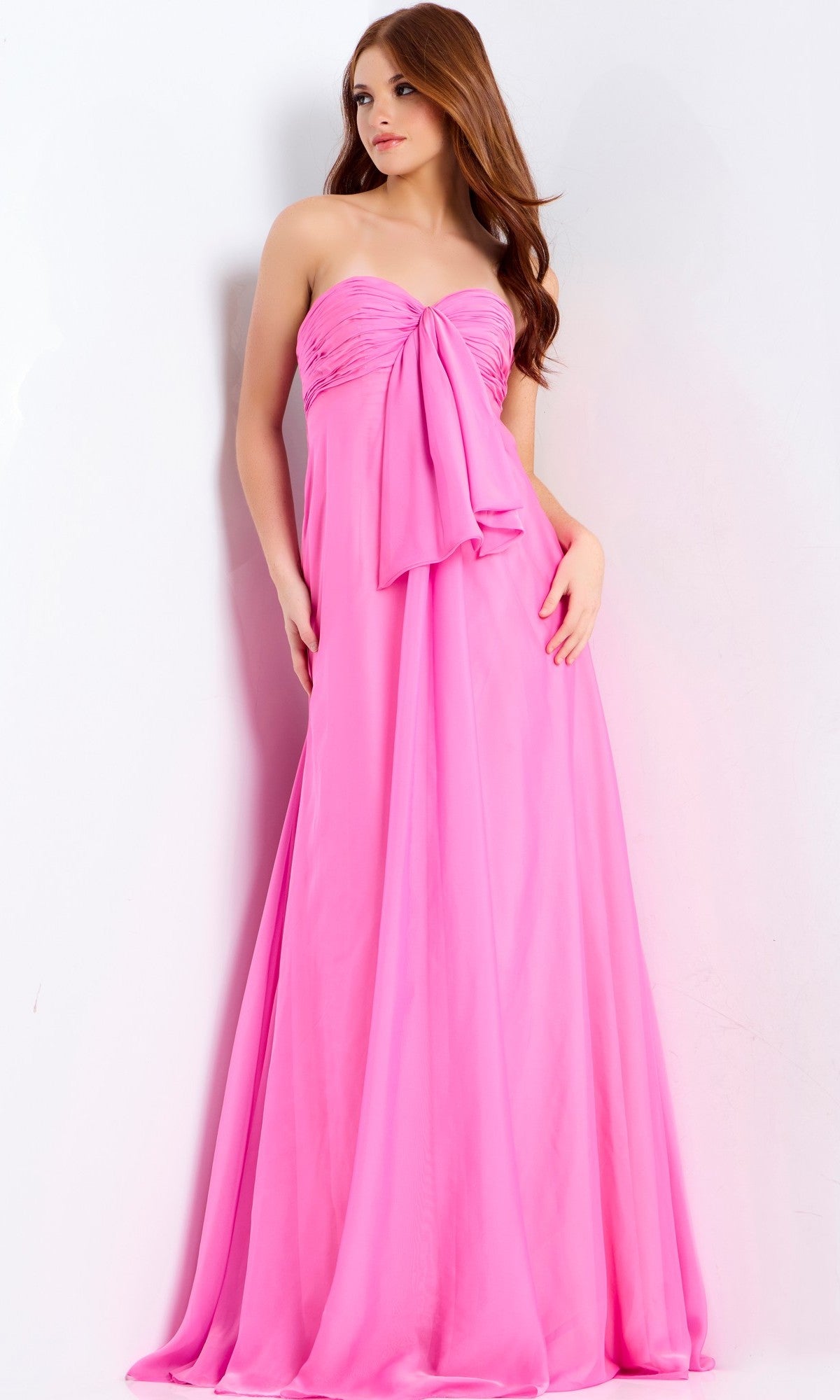A woman models the Jovani 47041 long prom dress, a strapless chiffon gown with a large bow on the bodice and an elegant floor-length skirt, standing against a plain white background.